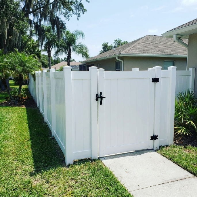 Black wrought-iron gate across a driveway with palm trees and a paved path behind it