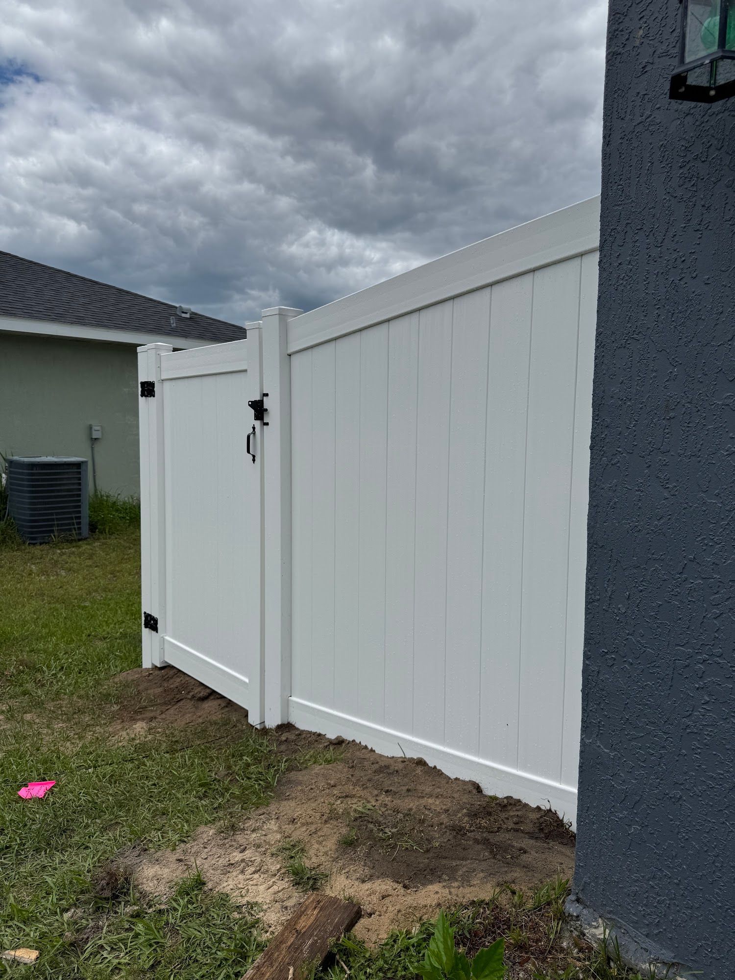 White vinyl fence and gate beside a dark gray house in a grassy yard under cloudy sky