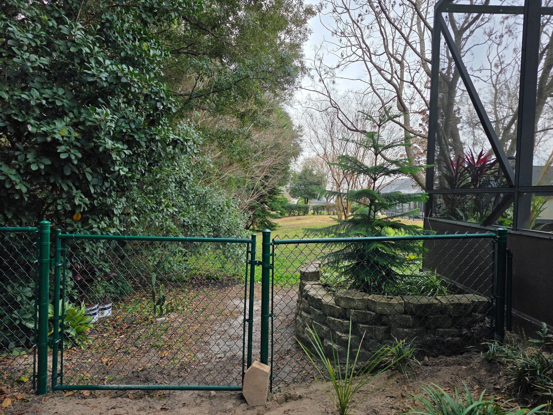 Black wrought-iron gate across a driveway with palm trees and a paved path behind it