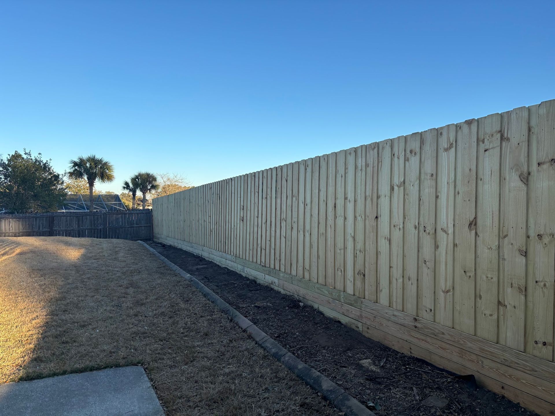 Long wooden fence beside a gravel path under a clear blue sky at sunset