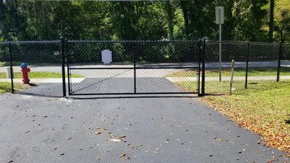 Closed chain-link gate blocking a paved path in a sunny park