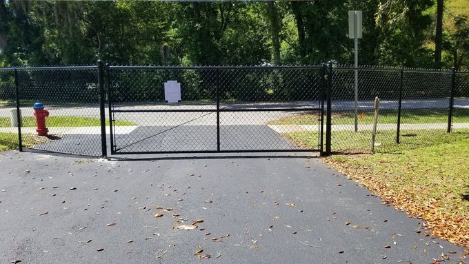 Closed chain-link gate blocking a paved path in a sunny park