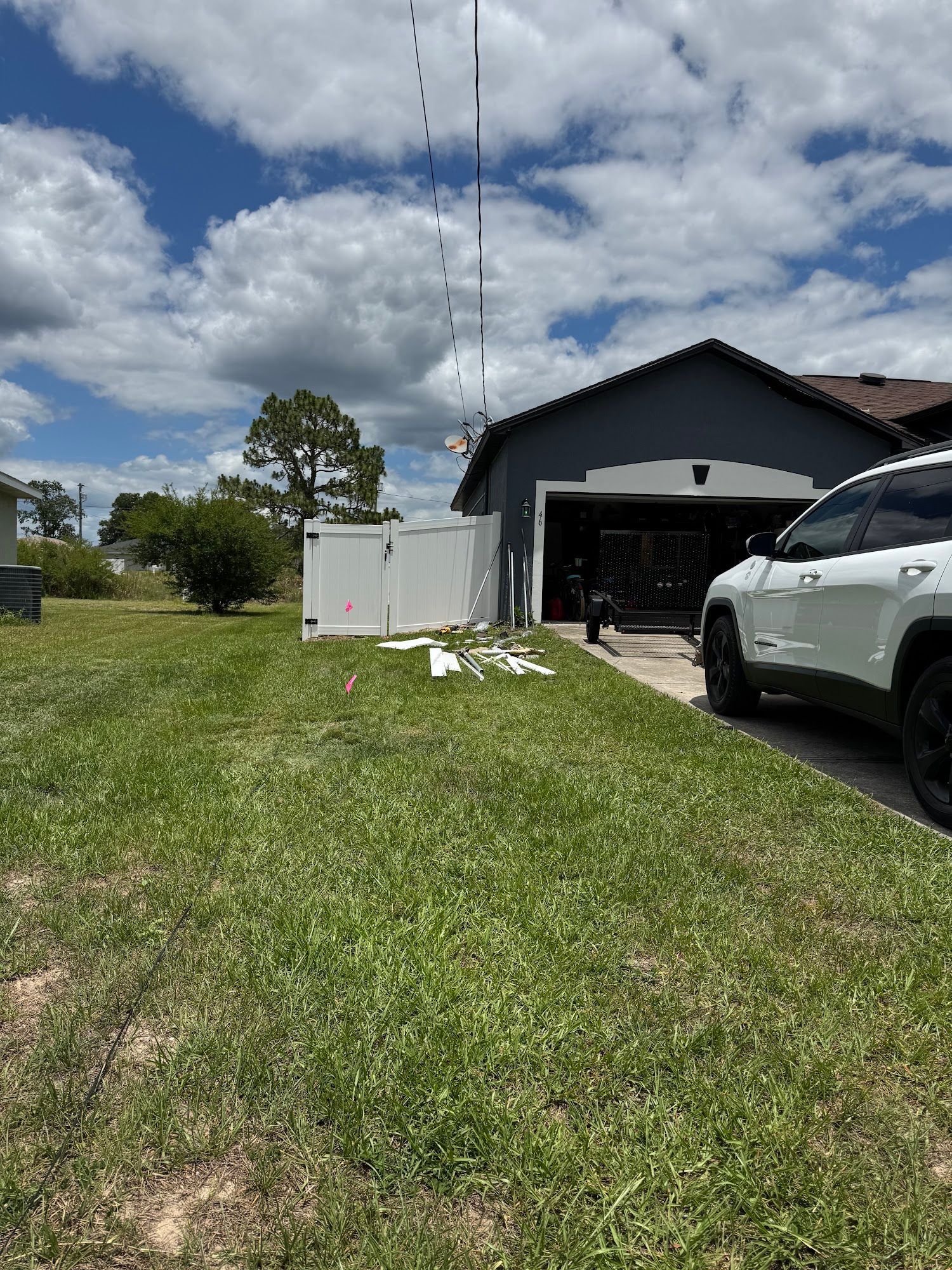 Suburban yard with white fence, small tower, dark garage, and white truck parked on grass under cloudy sky