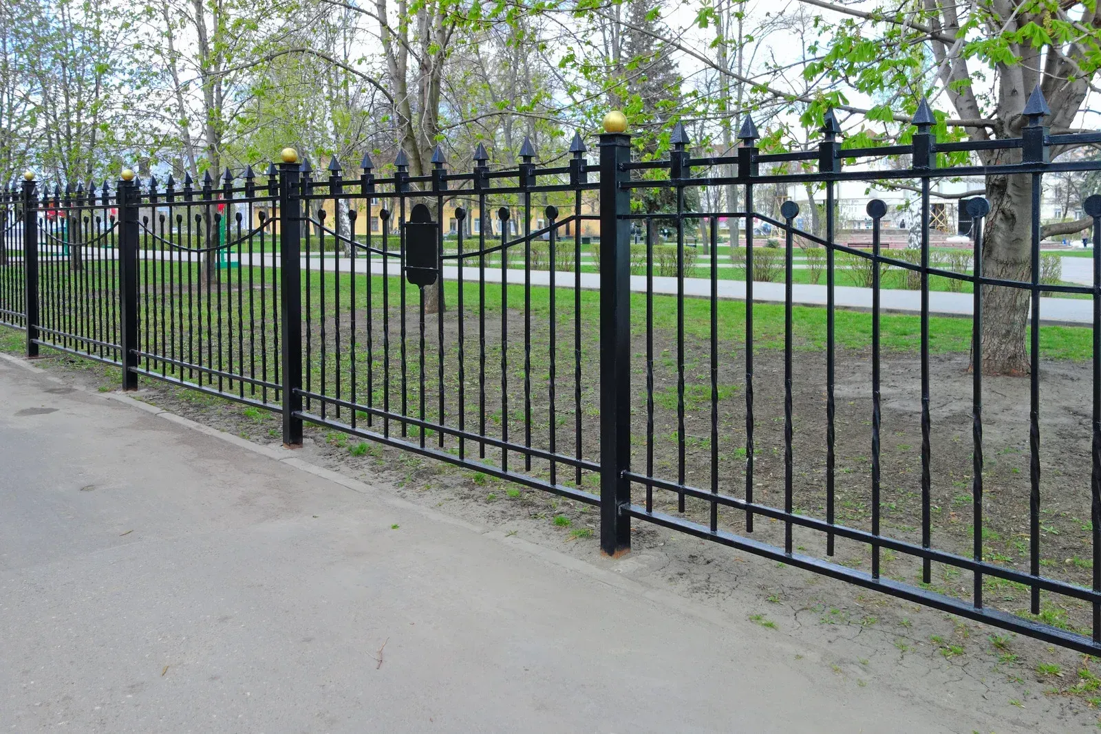 Black wrought-iron gate across a driveway with palm trees and a paved path behind it