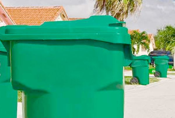 A man is spraying a green trash can with a spray bottle.