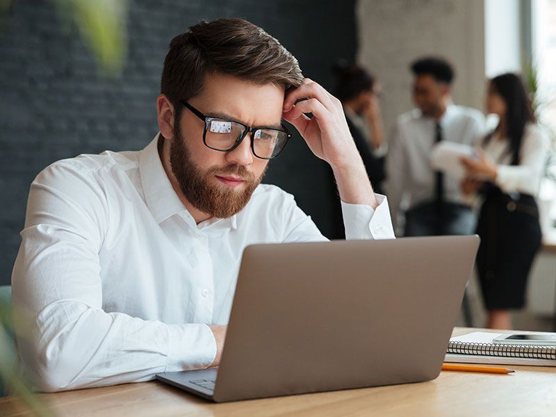 Um homem de óculos está sentado em uma mesa usando um laptop.