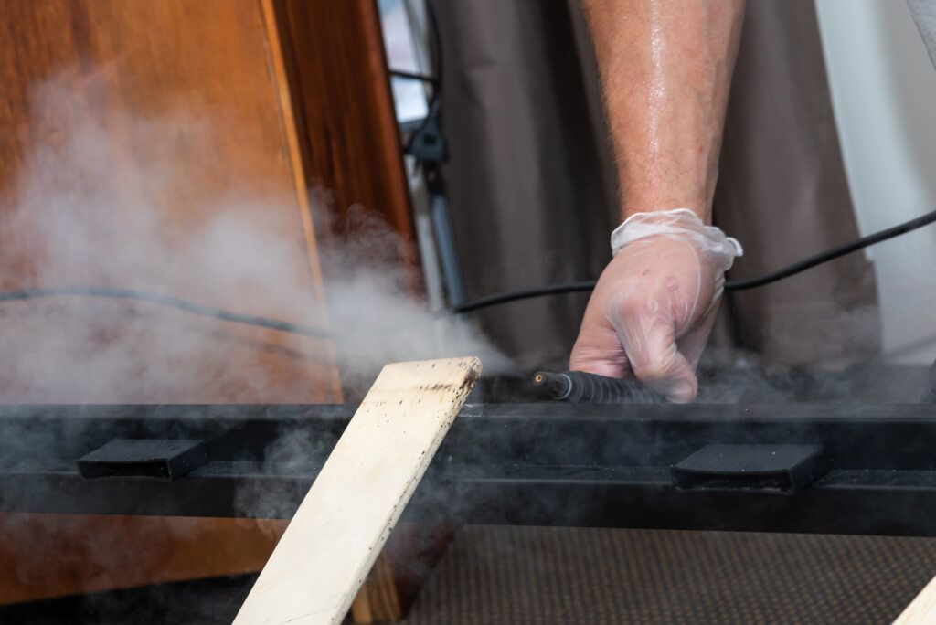 Person Using a Steam Cleaner on a Wooden Beam — NatureWise Pest Control In Port Macquarie, NSW