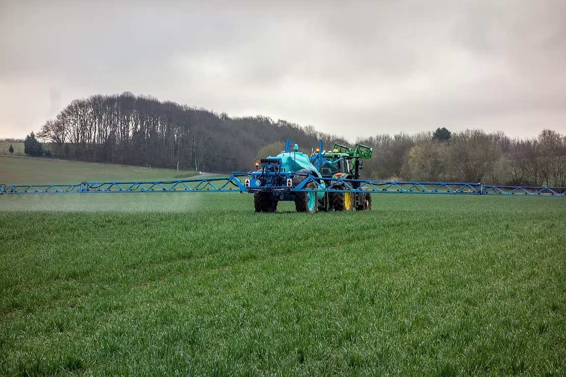 Blue Tractor Spraying a Field of Green Crops — NatureWise Pest Control In Port Macquarie, NSW