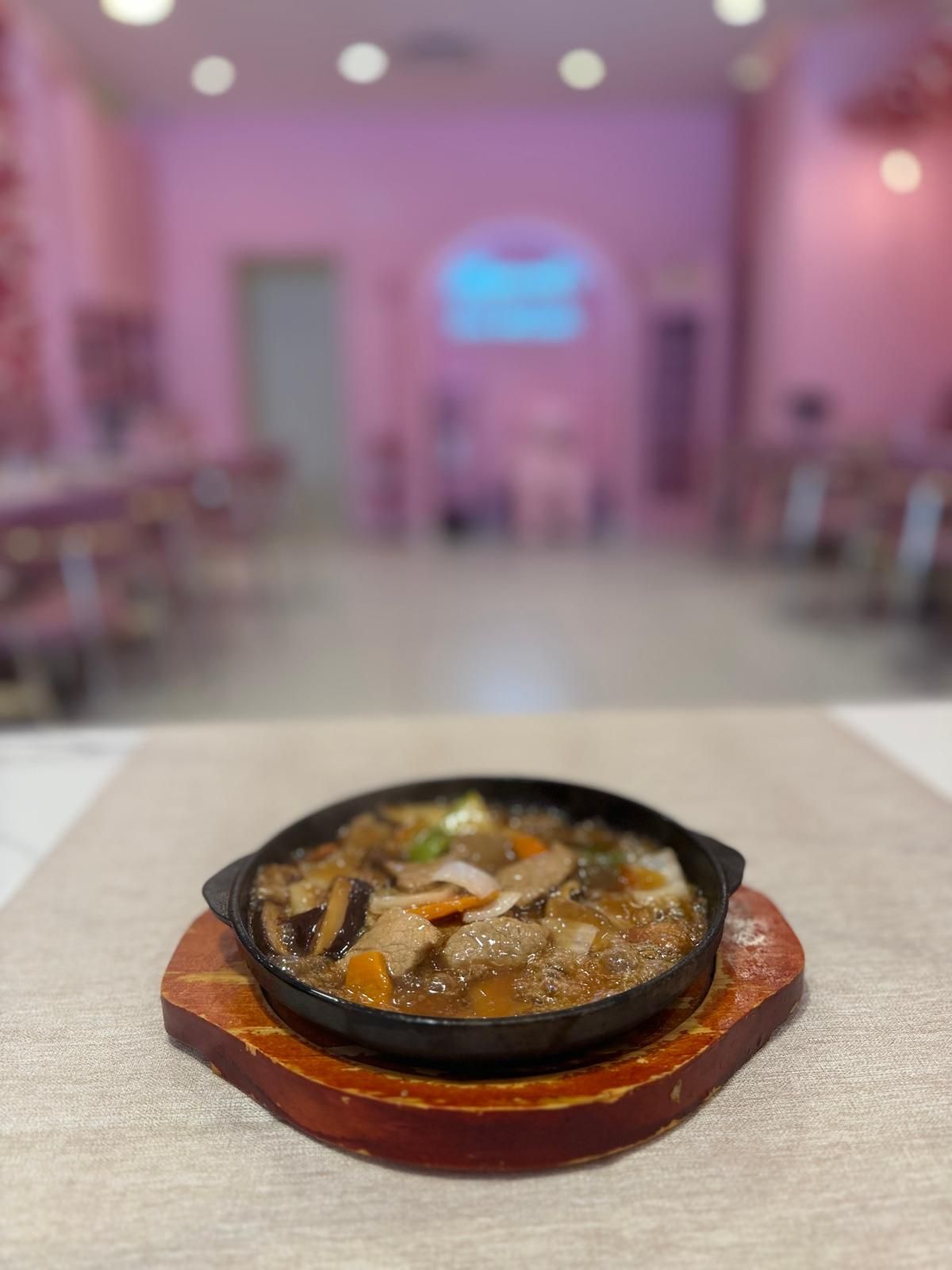 Padella di pietra rovente con carne mista e verdure, servita su un vassoio di legno in un ristorante dalla luce soffusa
