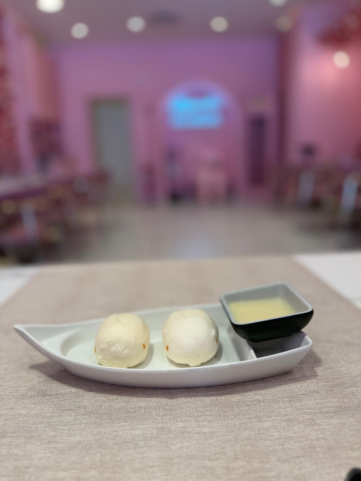 Due palline di gelato su un piatto bianco, con una piccola ciotolina quadrata per la salsa, su un tavolo in una stanza illuminata di rosa