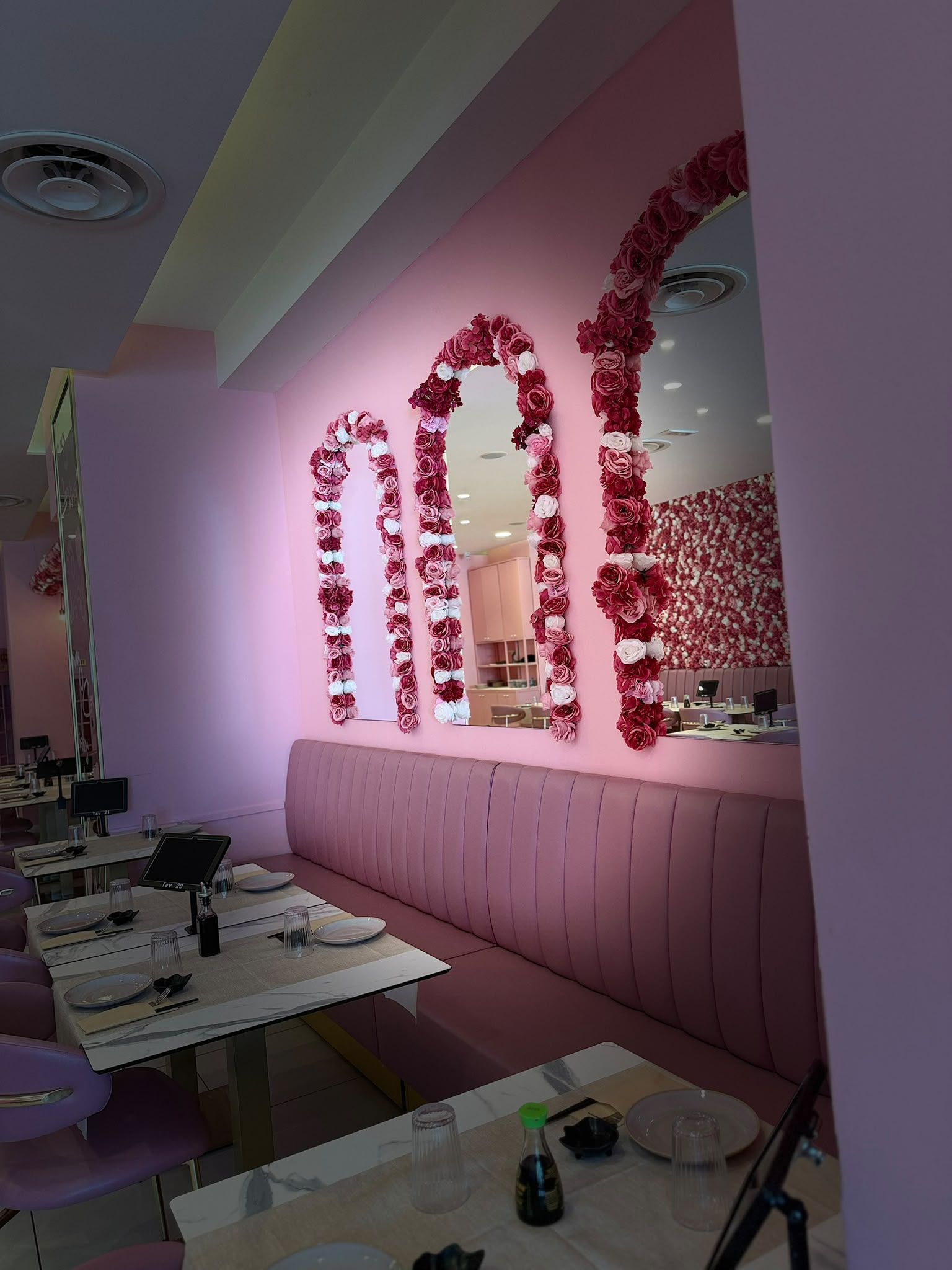 Sedute rosa per banchetti e decorazioni floreali alle pareti in una sala ristorante dalla luce soffusa.