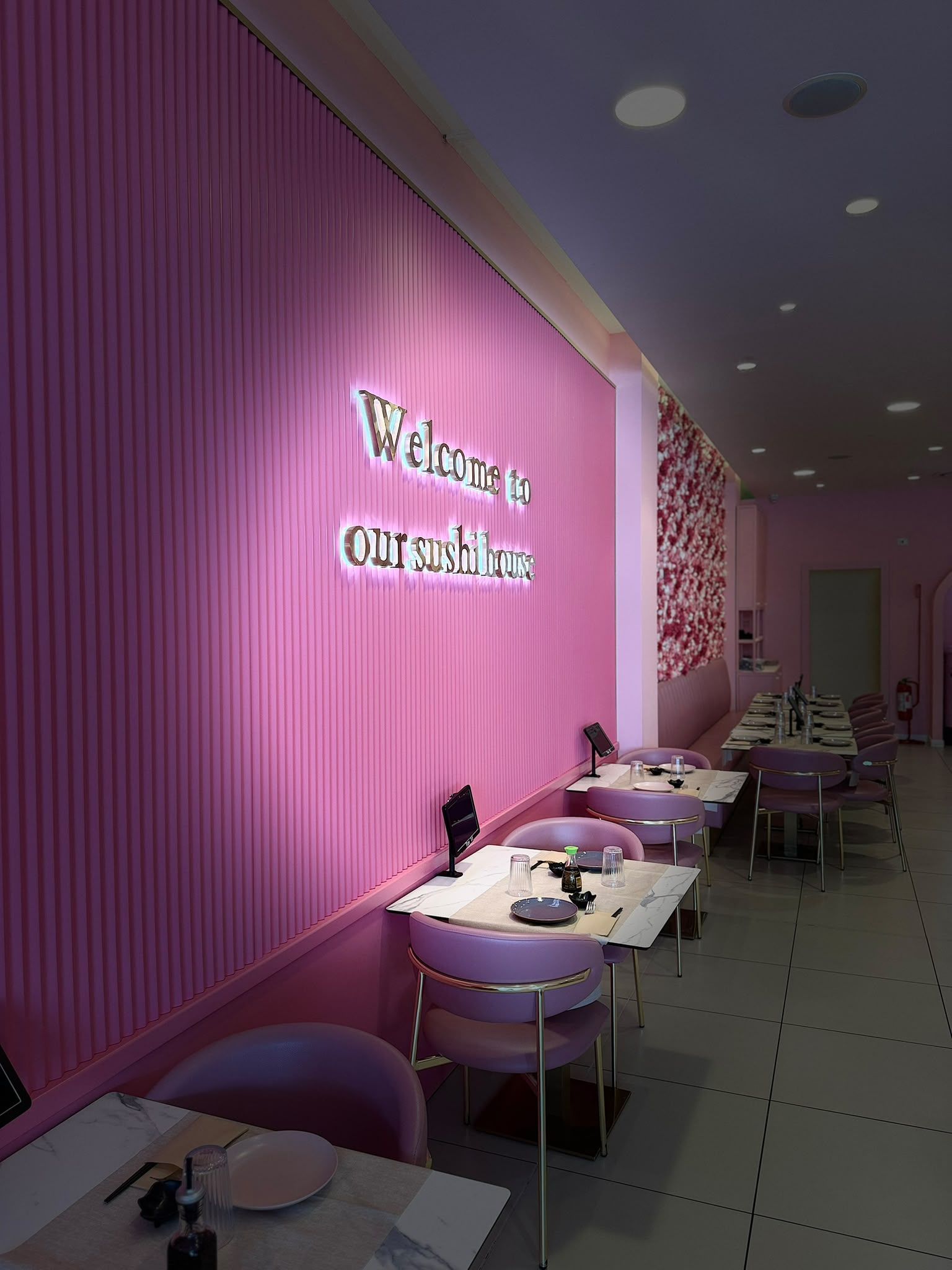 Interno di un bar sui toni del rosa, con tavolini lungo una parete su cui si legge “Welcome to Caffeine”