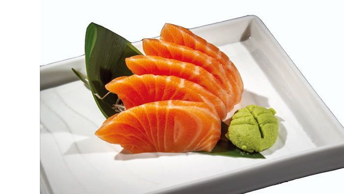 Sashimi di salmone a fette su un piatto bianco con wasabi e guarnizione