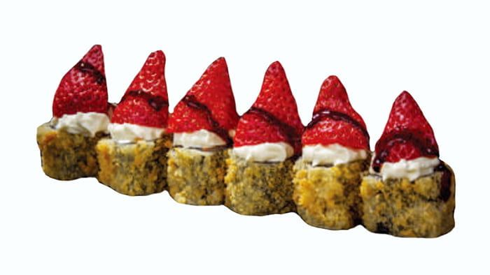 Rotolini di sushi dolci guarniti con fragole, disposti in fila su uno sfondo bianco