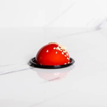 Dolce a forma di cupola rossa con codette bianche, su un piatto nero davanti a uno sfondo bianco