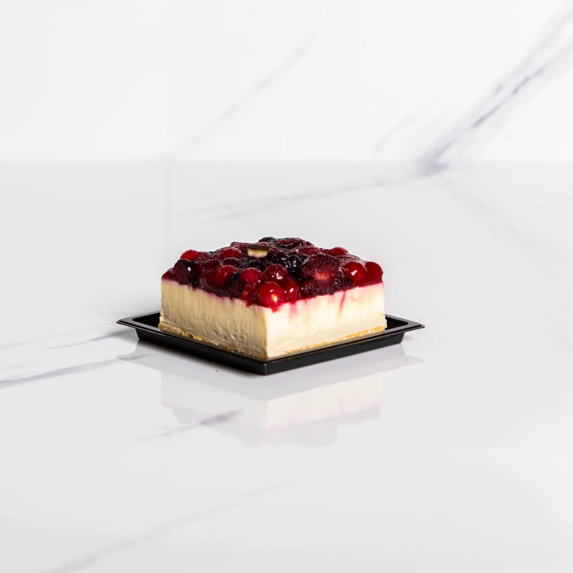 Cheesecake guarnita con frutti di bosco su un piatto nero, su uno sfondo di marmo bianco
