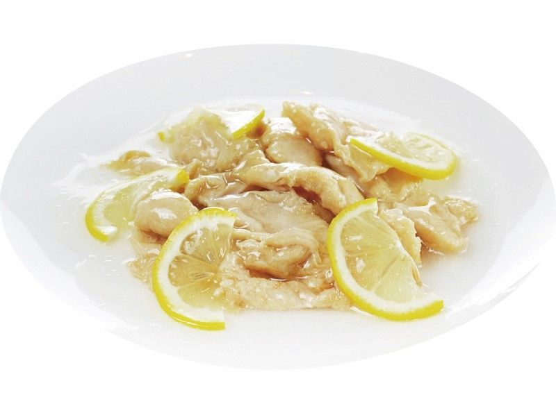 Bocconcini di pollo al limone guarniti con fettine di limone su un piatto bianco