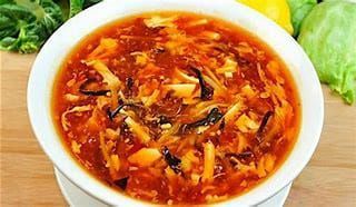 Ciotola bianca di zuppa di verdure rosse con ingredienti sminuzzati, su una superficie di legno con della lattuga accanto