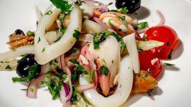 Insalata mista di mare con anelli di calamaro, gamberetti, olive, pomodorini e aromi, servita su un piatto bianco