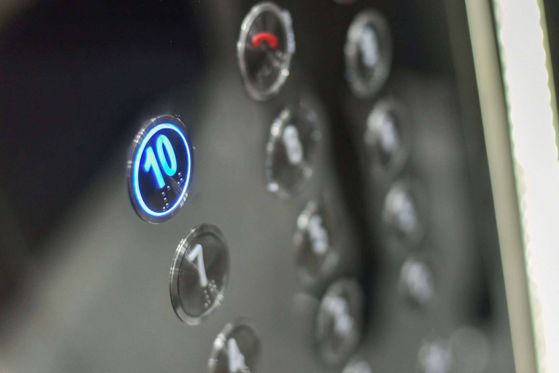 Close-up of elevator button panel, button 10 lit up with blue, other buttons blurred. Close-up of elevator button panel, button 10 lit up with blue, other buttons blurred.