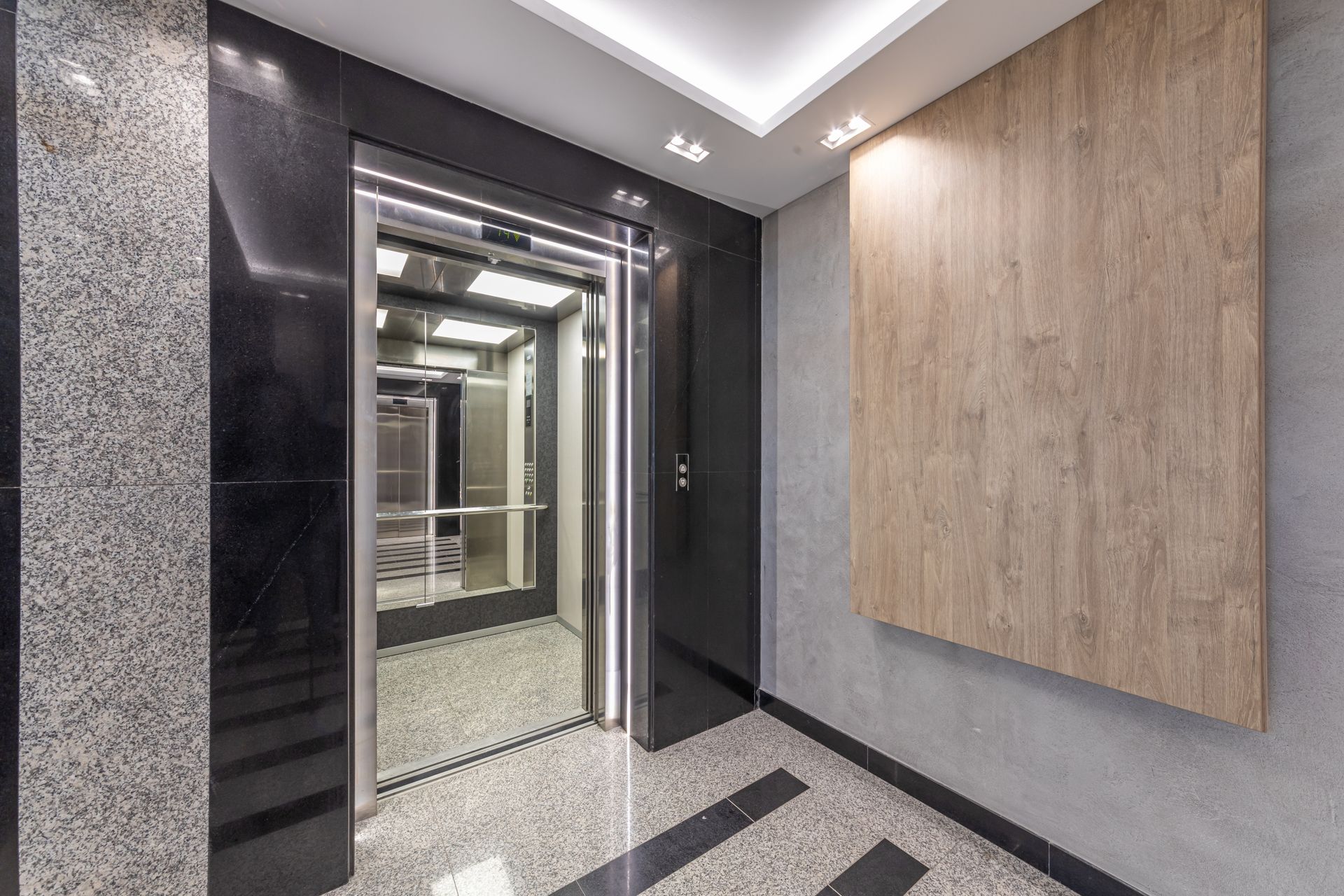 Elevator with open door, stainless steel trim, wood paneling, black and gray stone flooring. Elevator with open door, stainless steel trim, wood paneling, black and gray stone flooring.