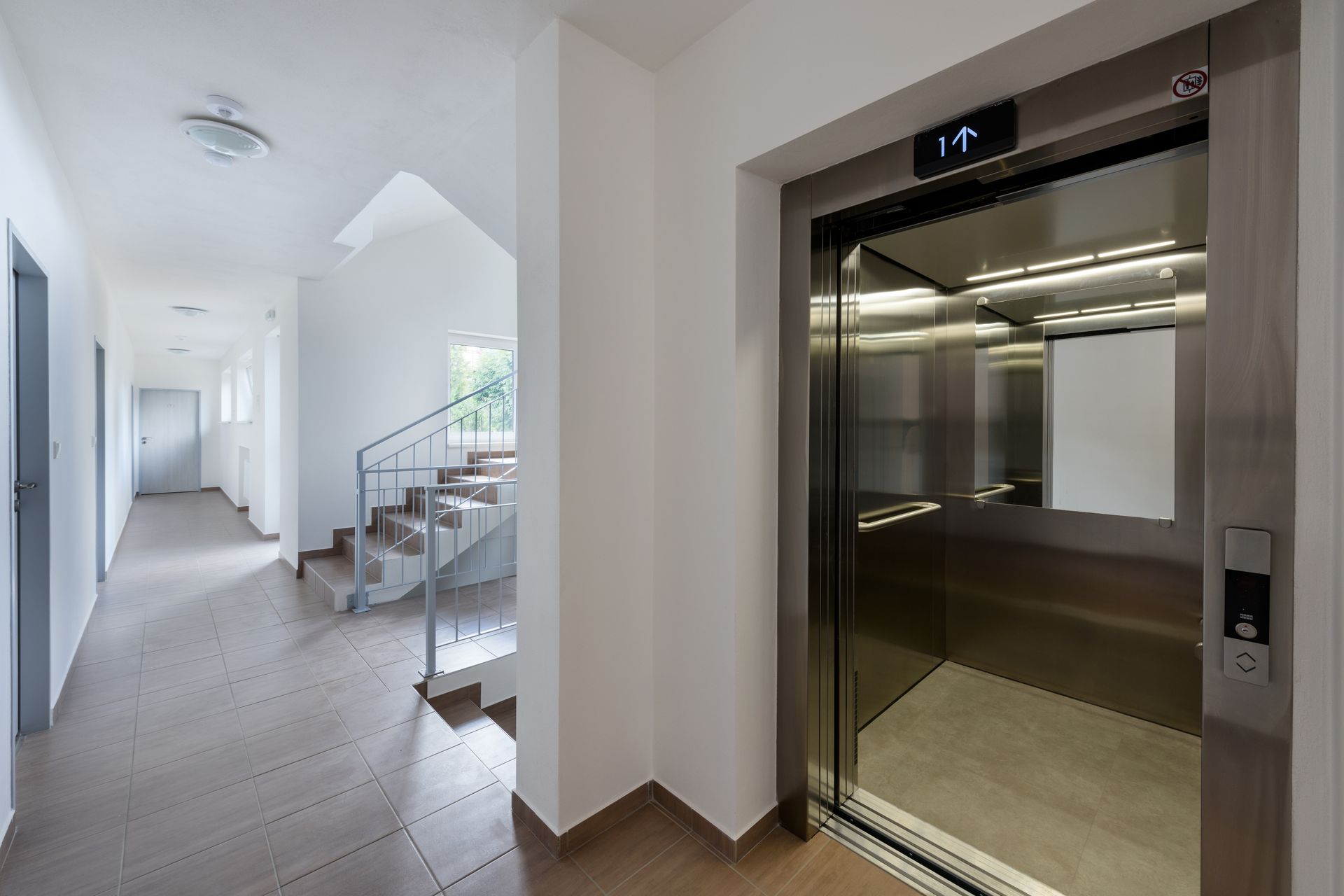 Hallway with elevator, stairs, and wooden floor. Elevator door open, stainless steel interior. Hallway with elevator, stairs, and wooden floor. Elevator door open, stainless steel interior.