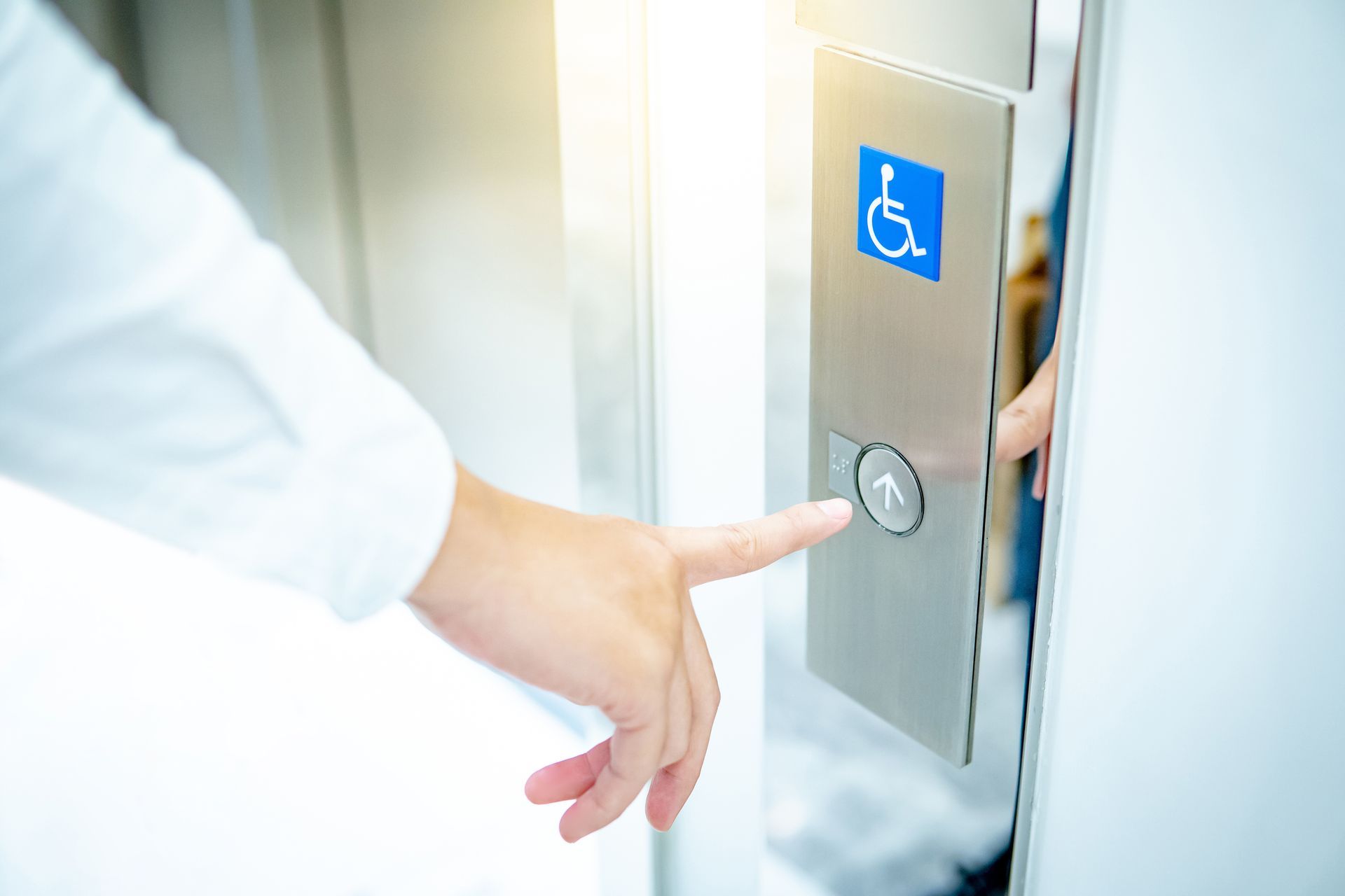 Person's finger pressing an elevator button with accessibility symbol. Silver metal panel. Bright light. Person's finger pressing an elevator button with accessibility symbol. Silver metal panel. Bright light.