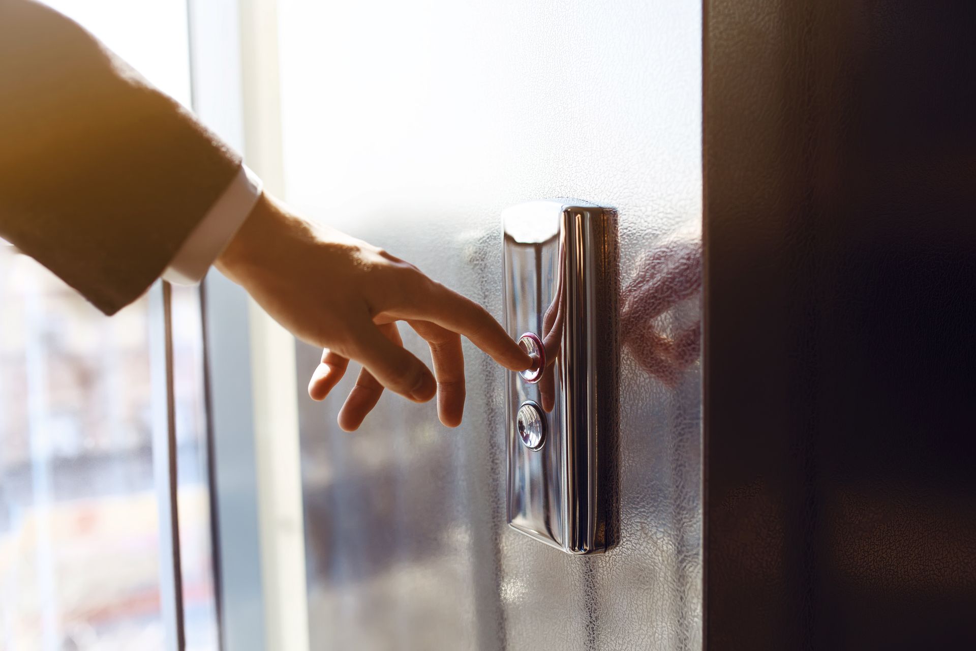 Hand pressing a silver elevator button next to a window. Sunlight illuminates the scene. Hand pressing a silver elevator button next to a window. Sunlight illuminates the scene.