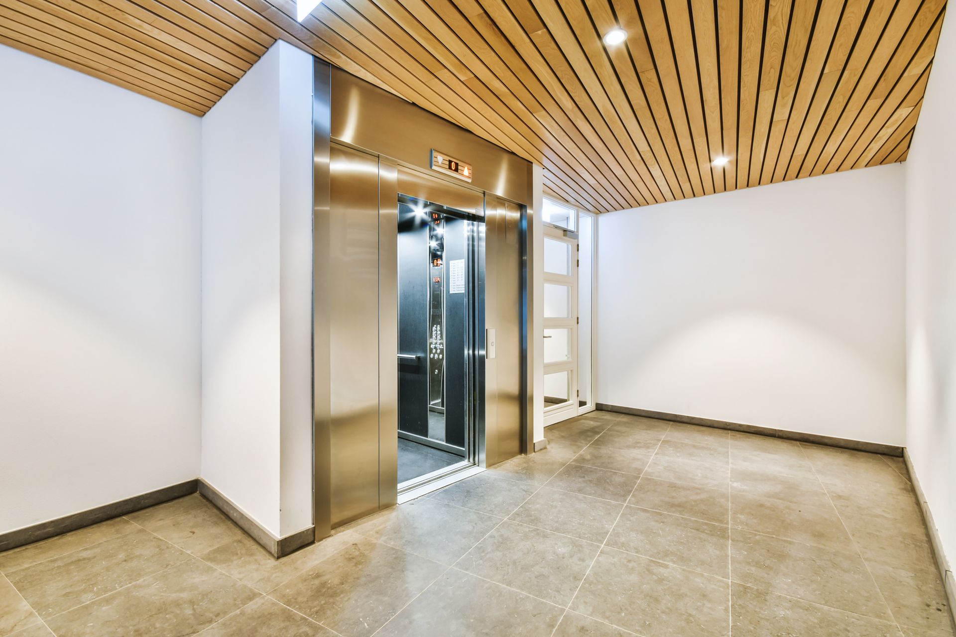 Hallway with elevator. Stainless steel doors, wood-paneled ceiling, gray tile floor, white walls. Hallway with elevator. Stainless steel doors, wood-paneled ceiling, gray tile floor, white walls.