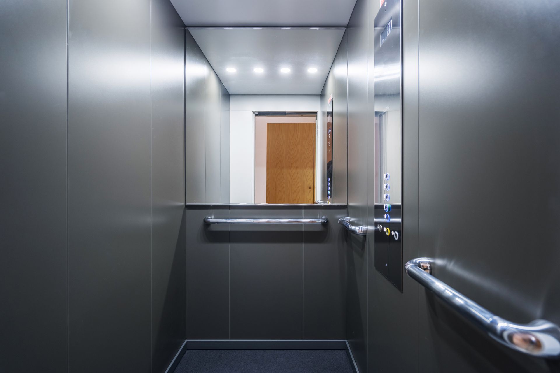 Interior of a modern elevator with silver walls, a mirror, and a door visible in the reflection. Interior of a modern elevator with silver walls, a mirror, and a door visible in the reflection.