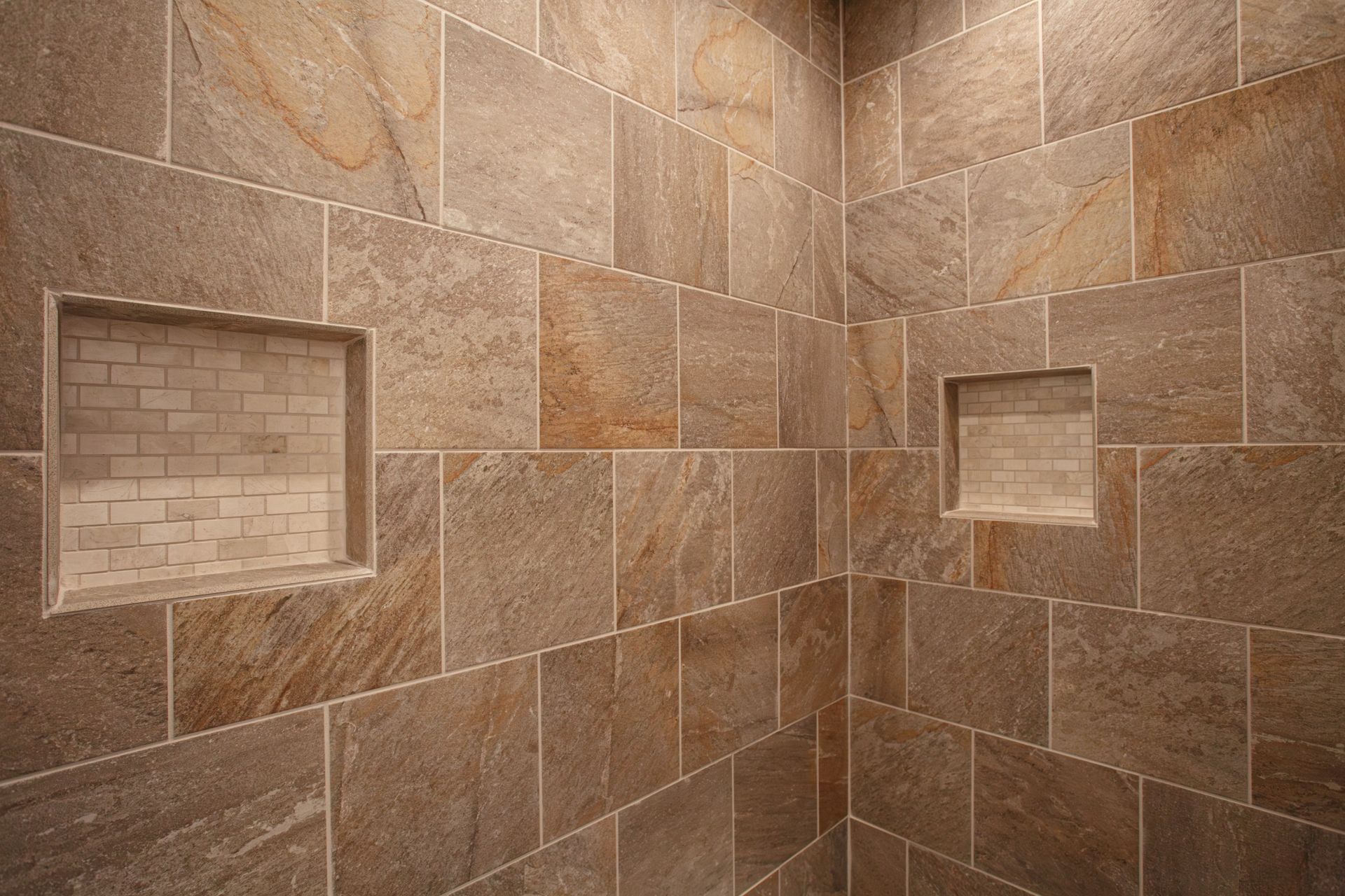 Stone-tiled shower corner with two recessed shelves on beige-brown walls Stone-tiled shower corner with two recessed shelves on beige-brown walls