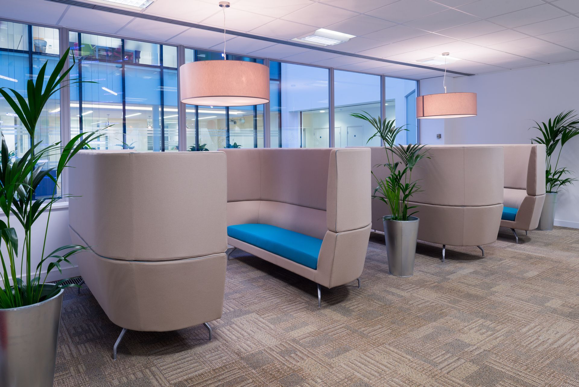 Modern office lounge with gray booths, blue seats, pendant lights, and large windows. Modern office lounge with gray booths, blue seats, pendant lights, and large windows.
