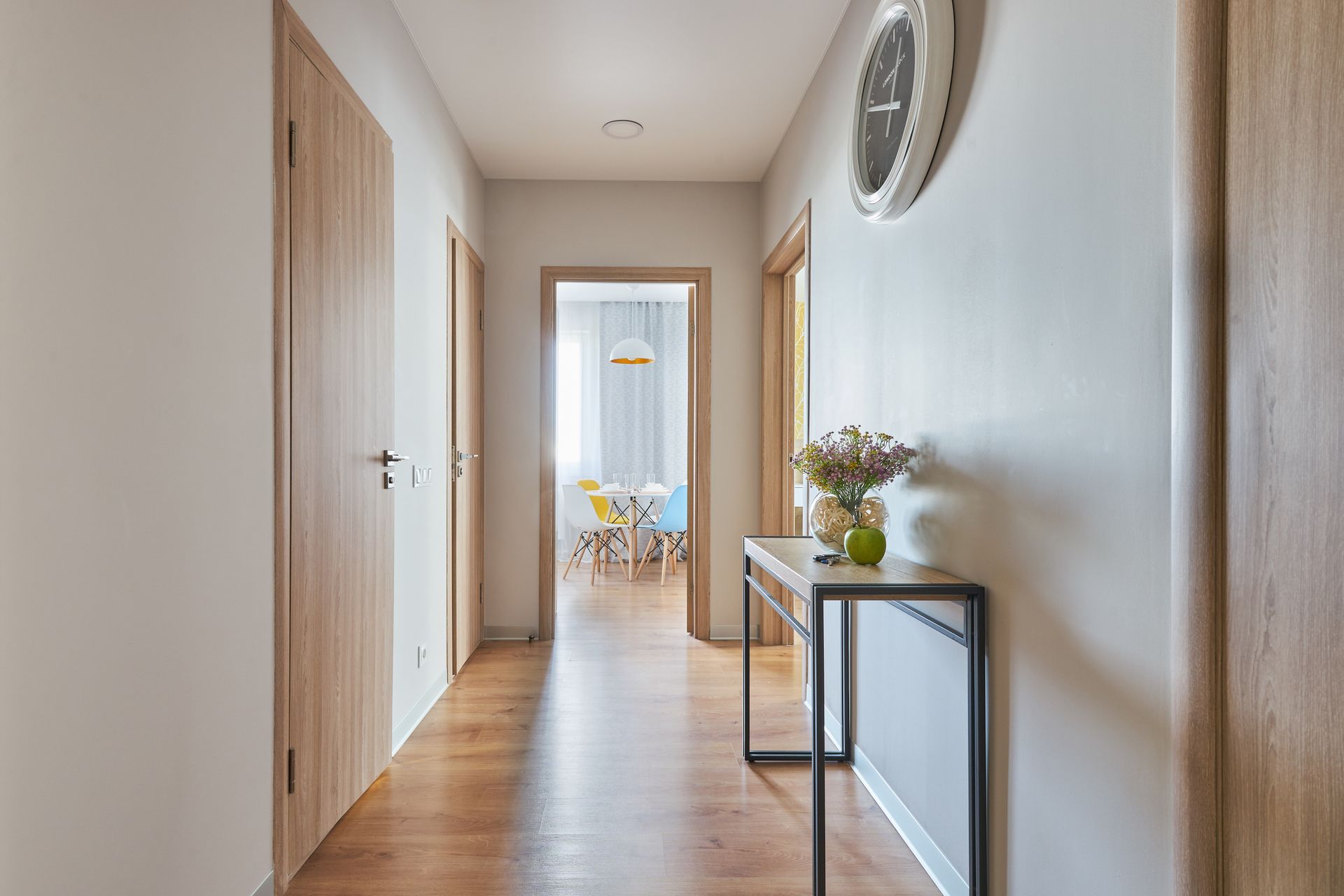 Bright hallway with wood floors, white walls, and a console table with flowers and a round mirror. Bright hallway with wood floors, white walls, and a console table with flowers and a round mirror.