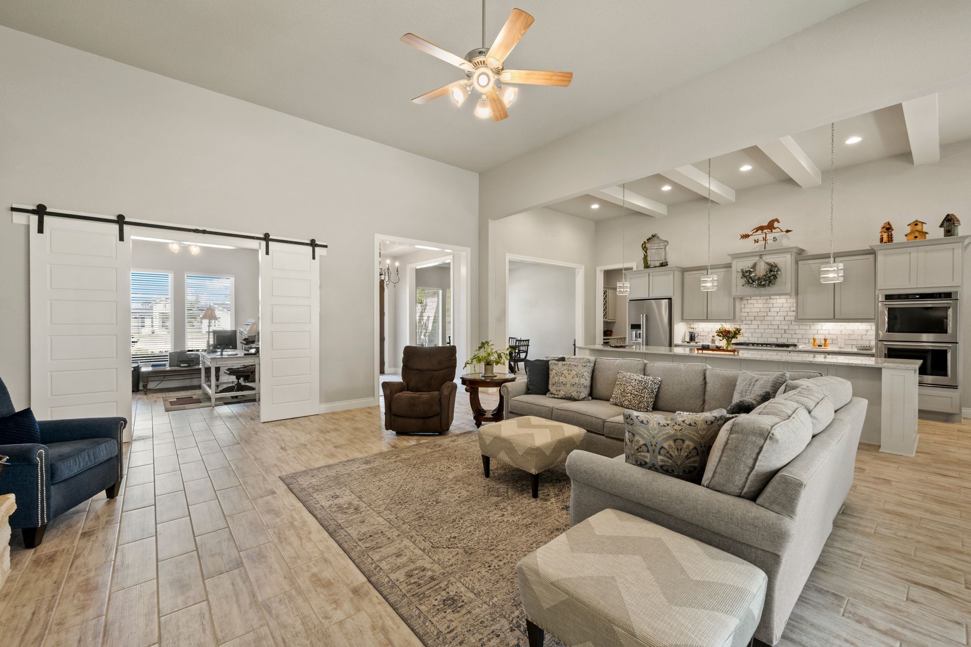 Bright open living room with gray sectional, chair, rug, and adjoining white kitchen with island Bright open living room with gray sectional, chair, rug, and adjoining white kitchen with island