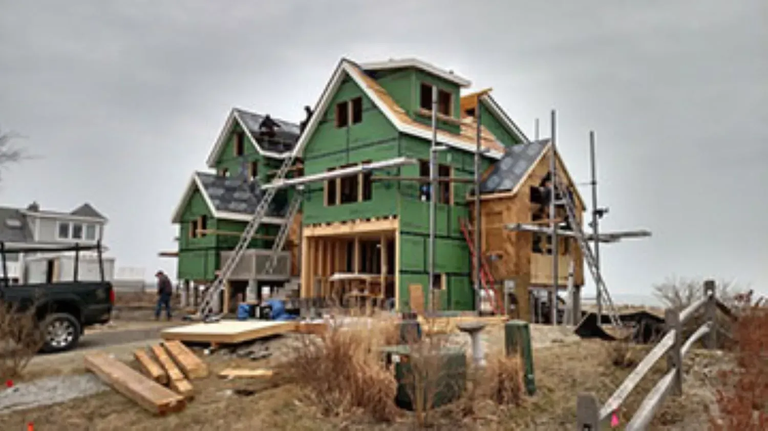A large house is being built in a field with a truck parked in front of it.