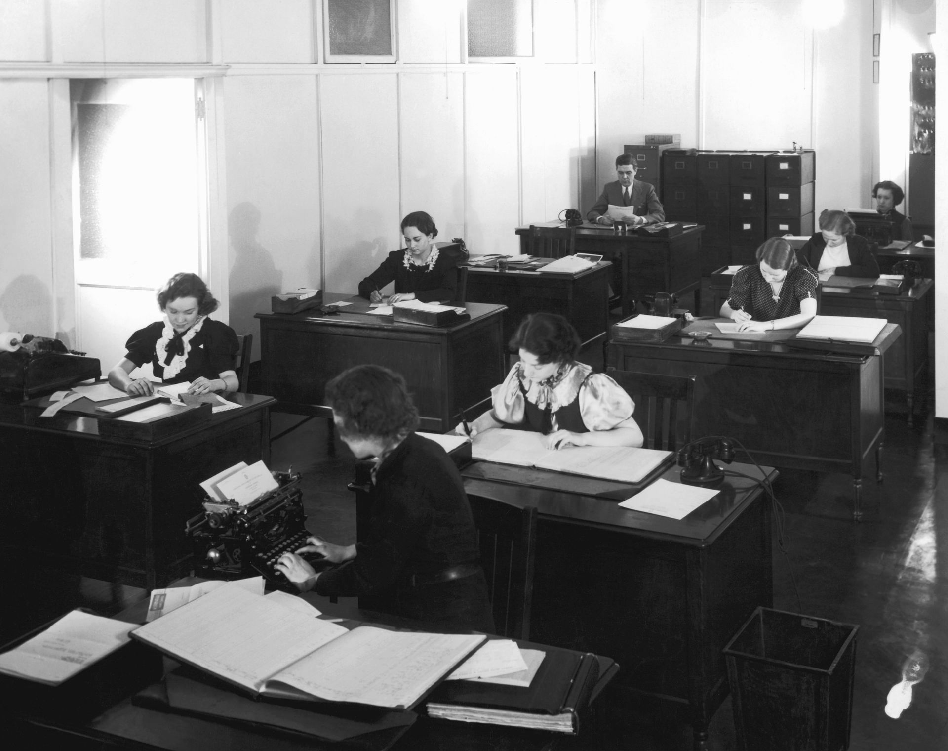 A black and white photo of people working in an office A black and white photo of people working in an office