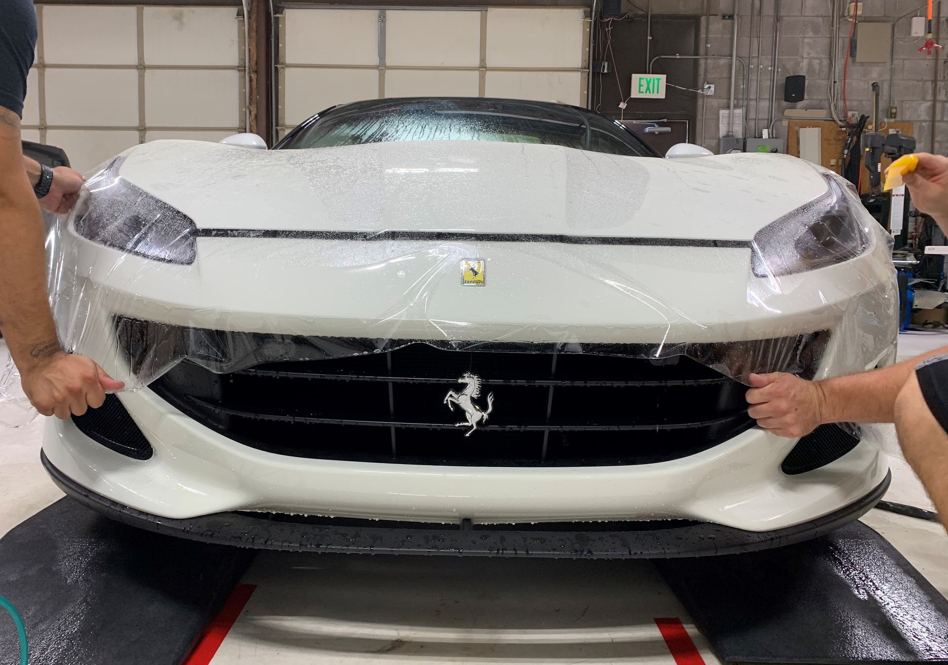 A man is covering the front of a white ferrari with plastic wrap.