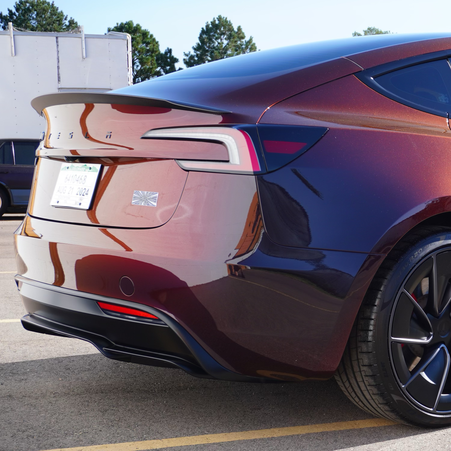 A red tesla model x is parked in a parking lot in front of a brick building.