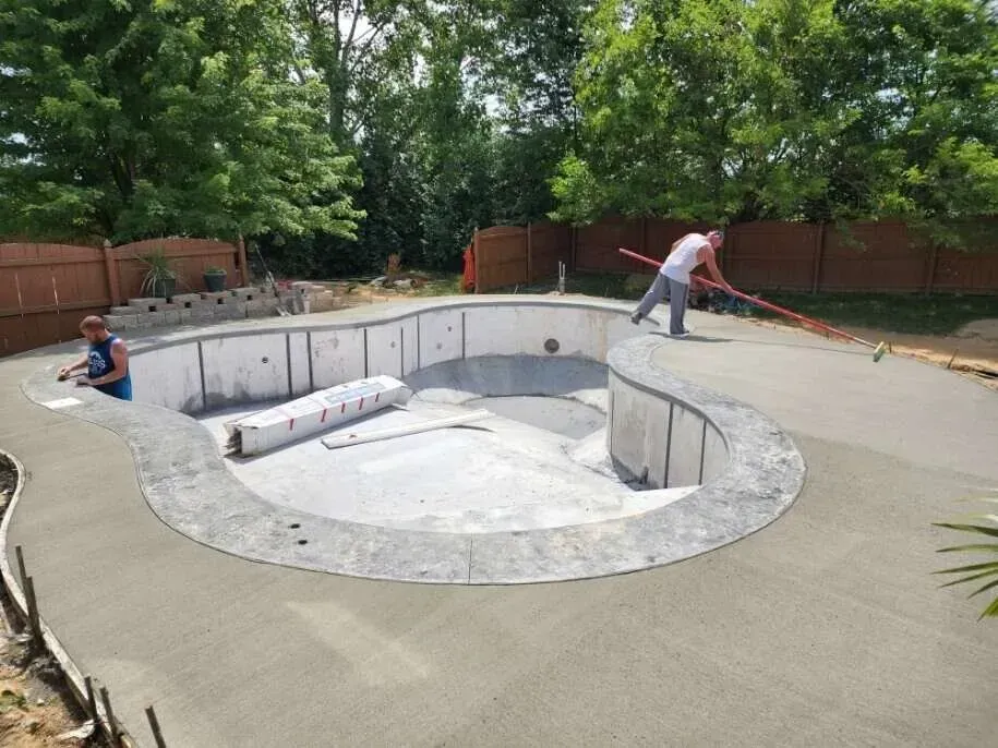 A man is working on a concrete pool in a backyard.