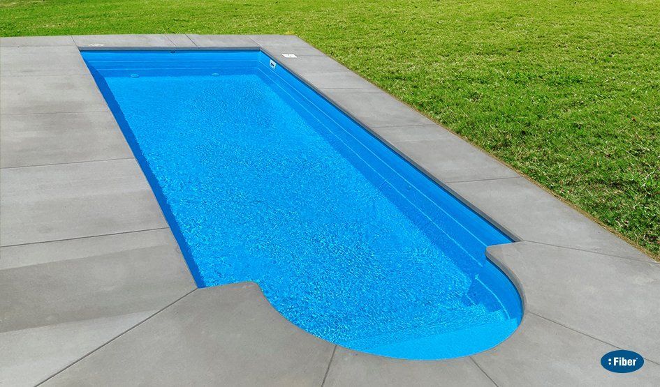 A blue swimming pool is surrounded by grass and concrete