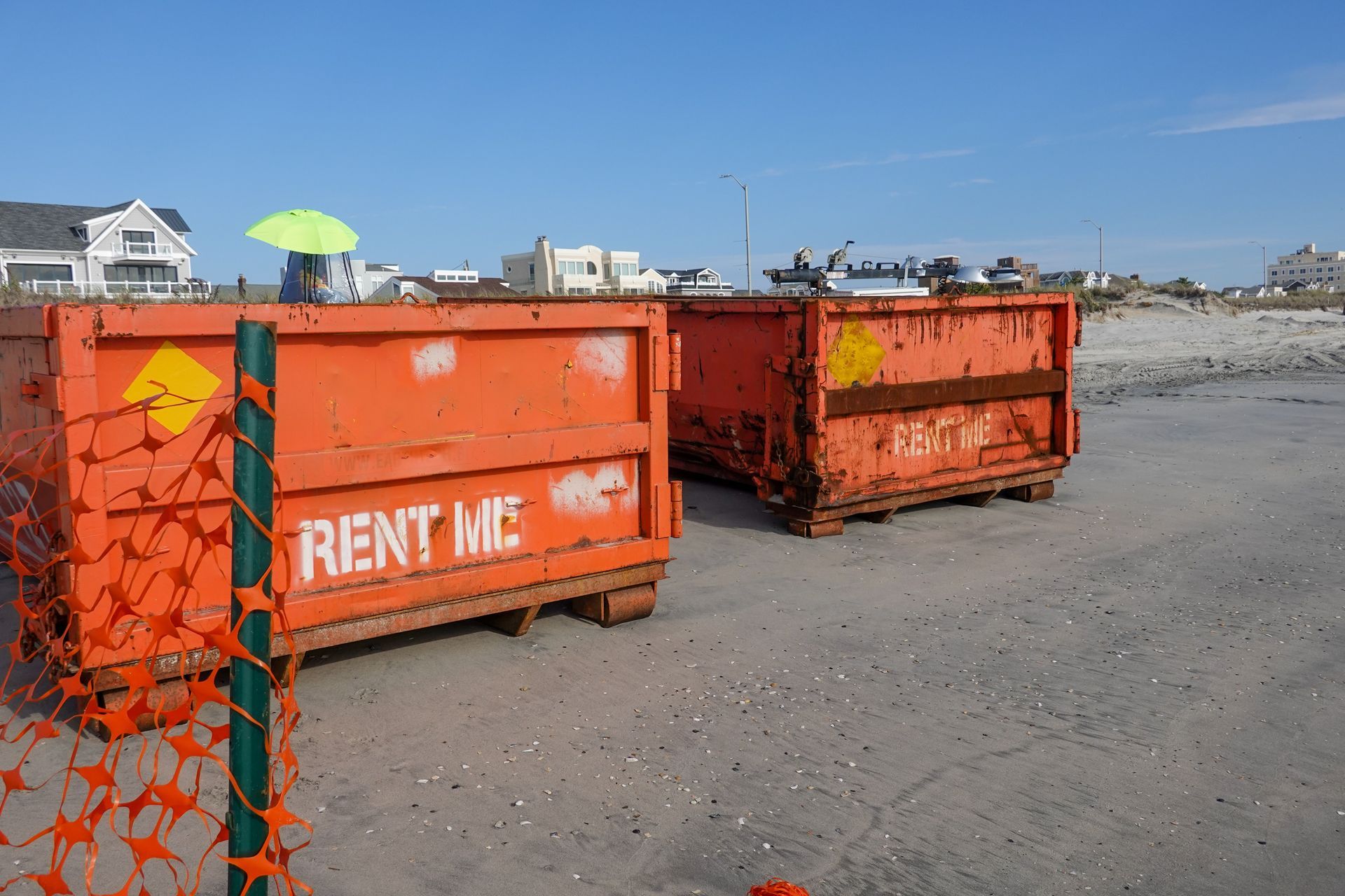 Two orange dumpsters are sitting next to each other in a dirt field.