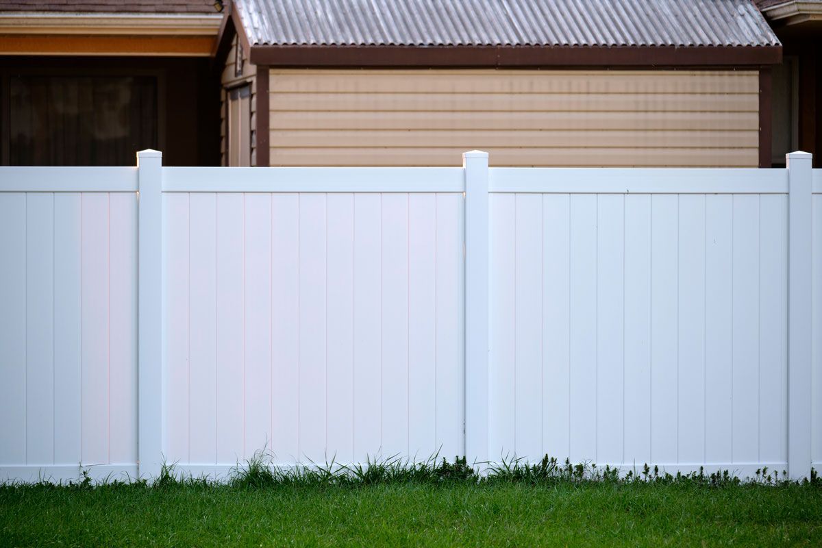 A white vinyl fence surrounds a lush green yard in front of a house.
