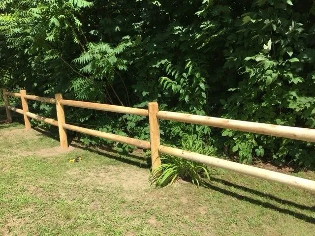 A wooden fence surrounds a grassy area with trees in the background