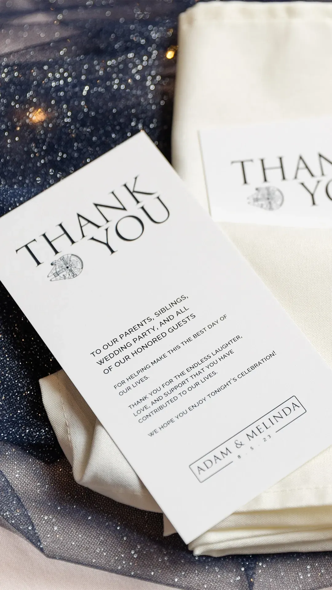 Two white thank-you cards on a dark starry fabric with folded cream napkins