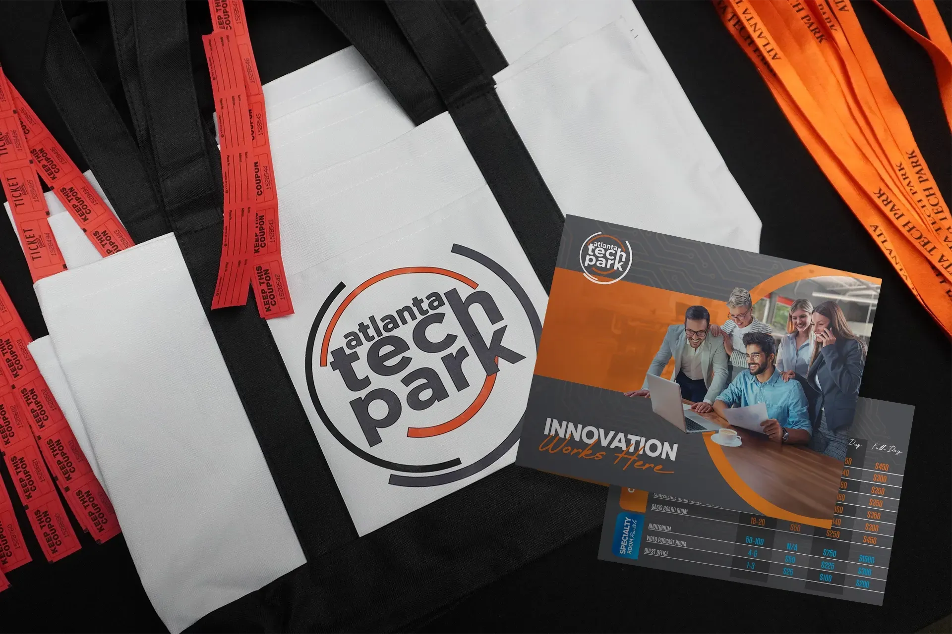 Black tote bags, red and orange lanyards, and tech park event brochures on a white surface