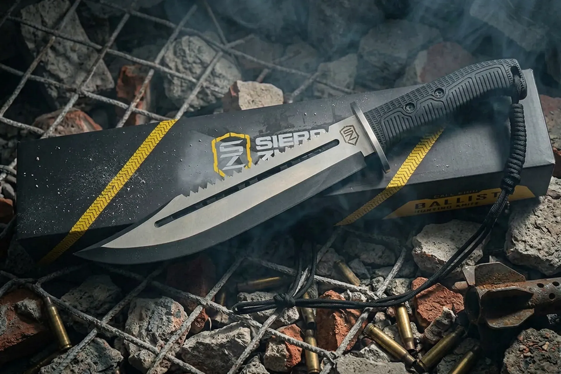Folded gray and black tactical knife on rocks and twigs, with yellow stripes and a serrated blade.