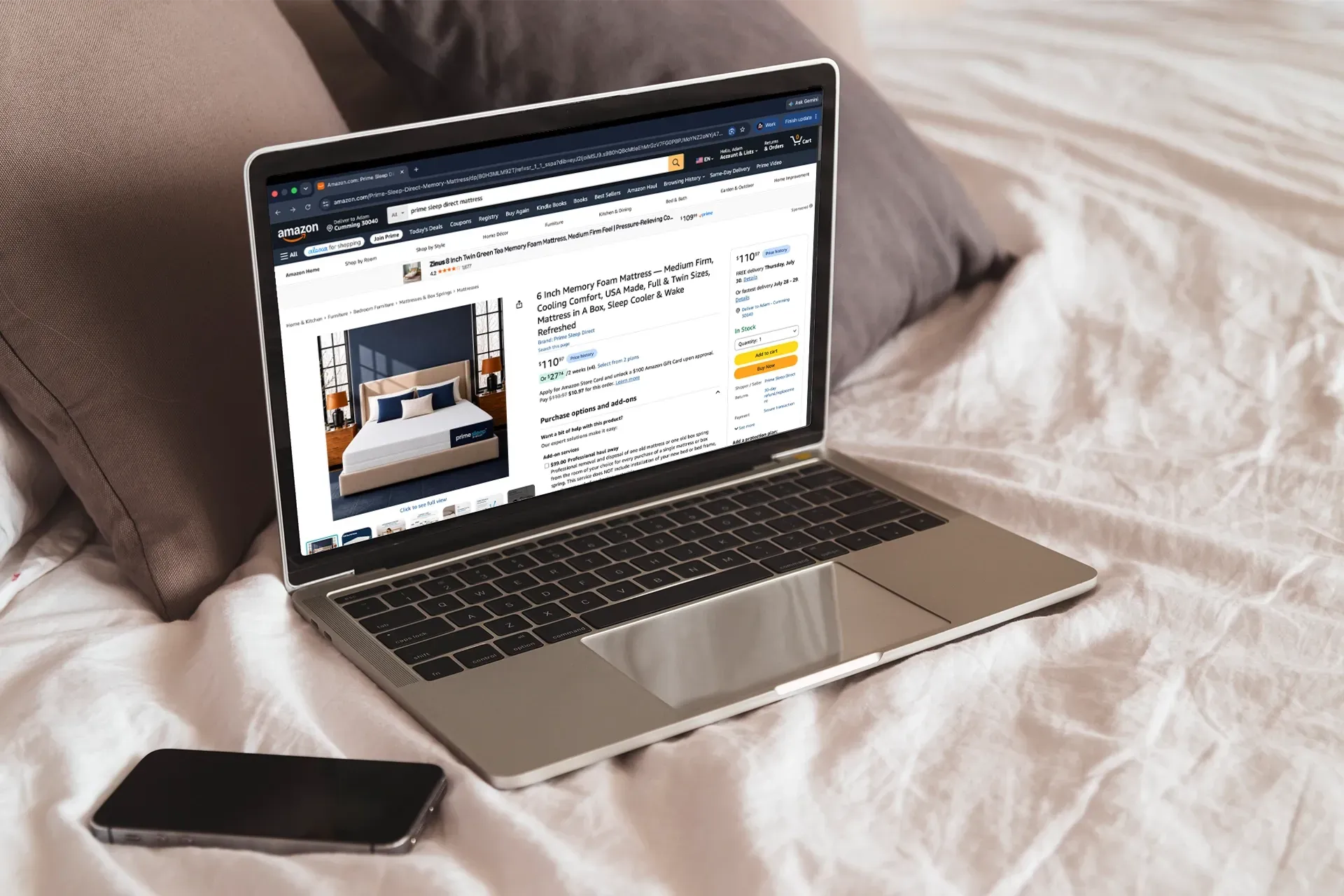 Laptop on a bed displaying a website, with a smartphone beside it.