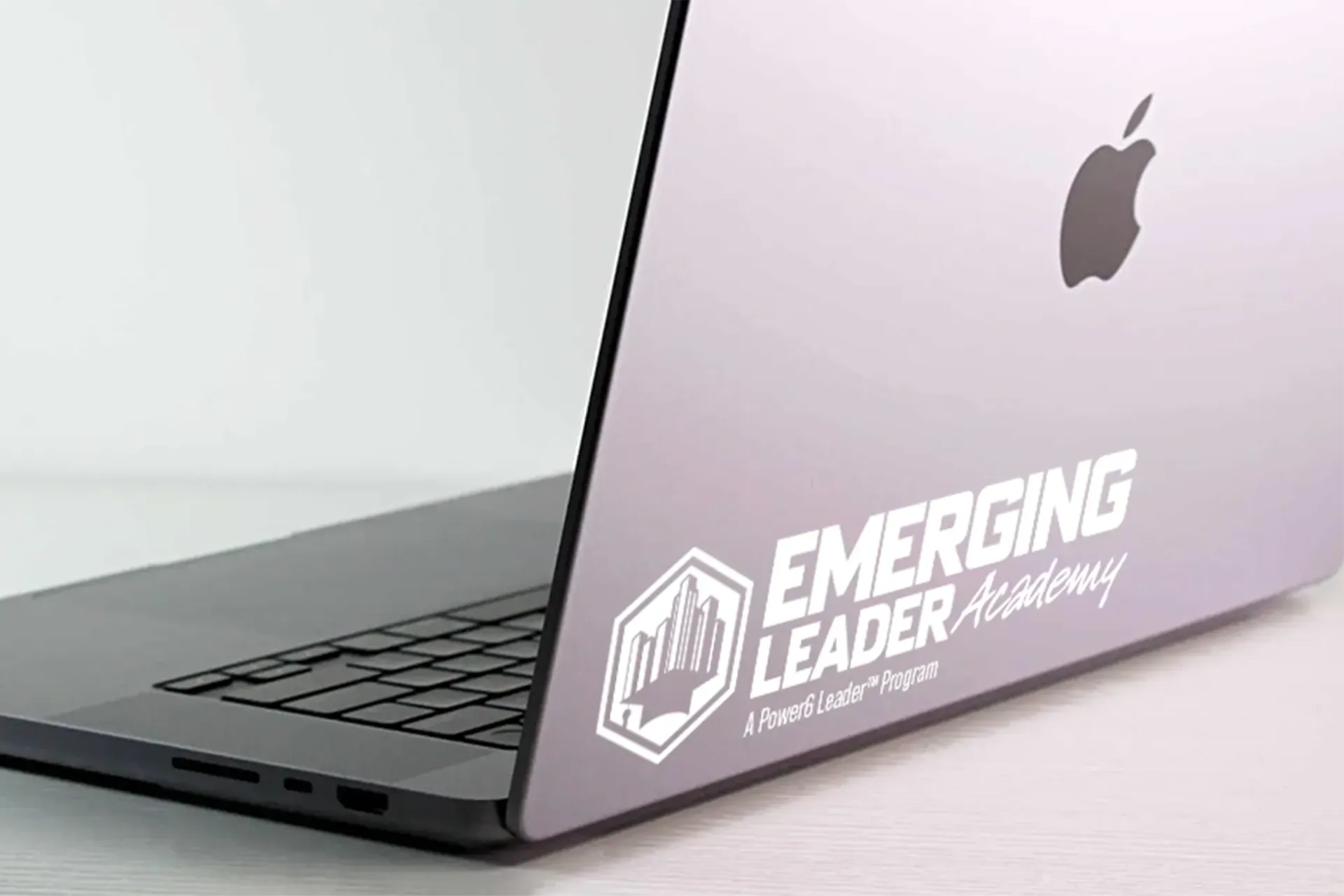 Silver MacBook with “Emerging Leader” sticker on the lid, open on a light desk