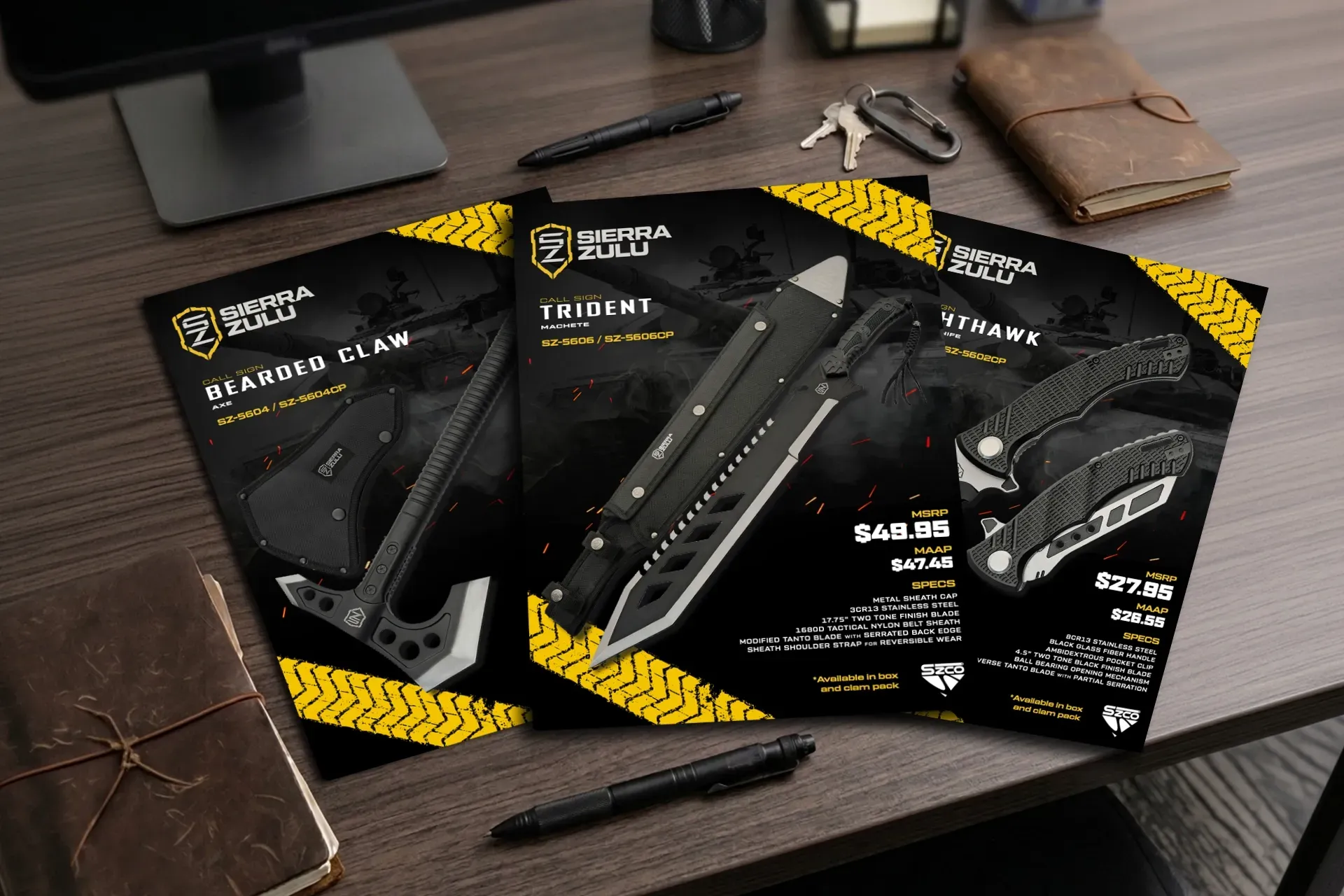 Three black folding knives in packaging on a wooden desk with a laptop and wallet nearby