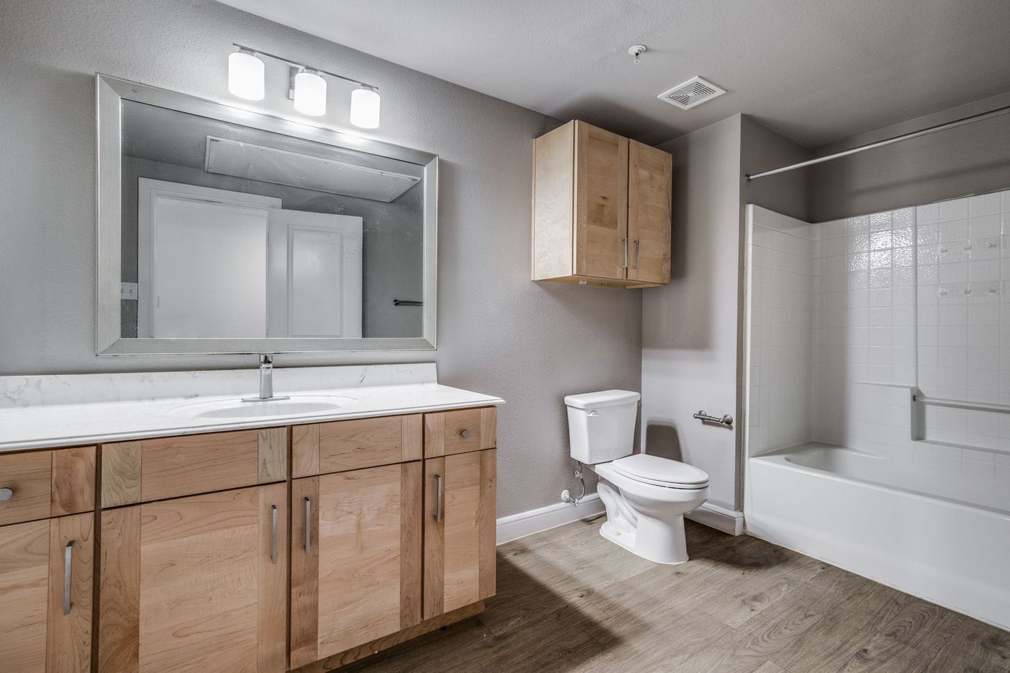 Bathroom with light wood vanity, toilet, tub/shower, and gray walls.